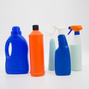 Cinque flaconi e spruzzini in plastica di vari colori (blu, arancione, azzurro, verde chiaro) disposti su sfondo bianco.