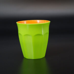 Bicchiere in plastica bicolore verde acido all'esterno e arancione all'interno, con superficie facettata, su sfondo scuro.