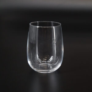 Bicchiere tumbler trasparente senza stelo, vuoto, su sfondo scuro, con riflessi di luce sulla superficie del vetro.