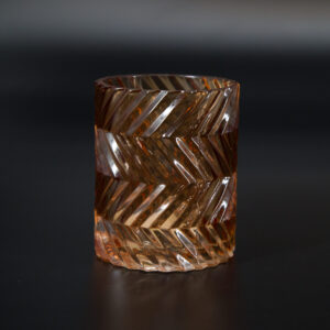 Vaso o portacandele cilindrico in vetro ambrato con una texture esterna a motivo di spina di pesce, su sfondo scuro.