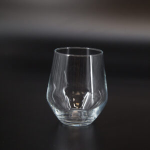 Bicchiere tumbler in vetro trasparente, vuoto, con base spessa e bordo liscio, su sfondo scuro.