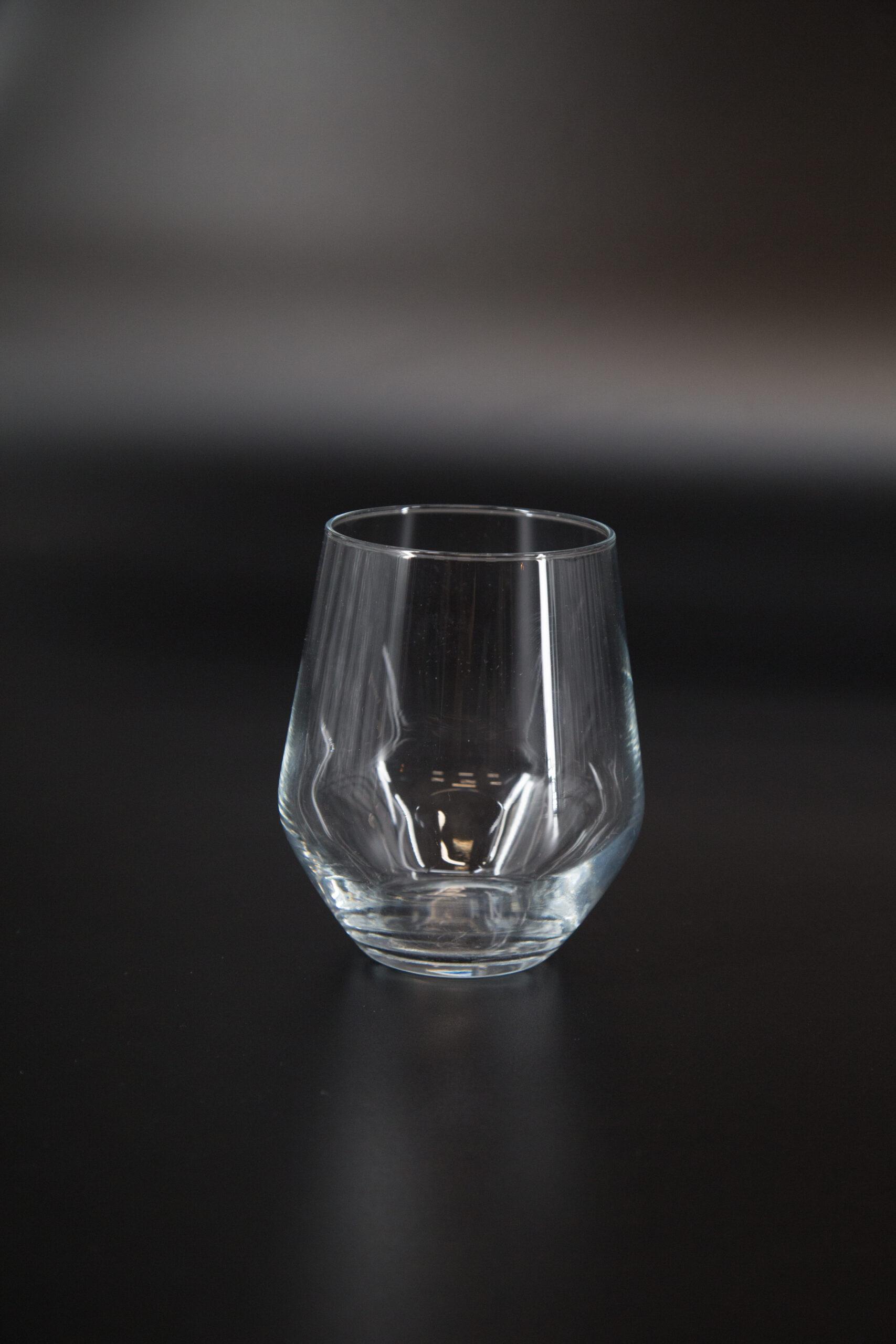 Bicchiere tumbler in vetro trasparente, vuoto, con base spessa e bordo liscio, su sfondo scuro.