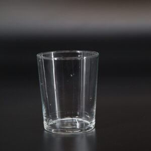 Un bicchiere tumbler in vetro trasparente, vuoto, posizionato centralmente su uno sfondo scuro e sfumato.