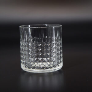 Bicchiere tumbler in vetro trasparente con motivo a rombi intagliato, posizionato su sfondo scuro per evidenziarne la texture.