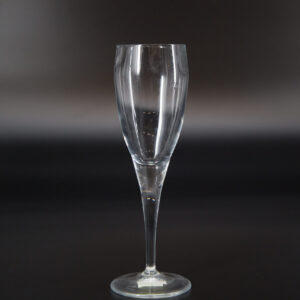Calice flute in vetro trasparente con stelo sottile e base circolare, fotografato su sfondo scuro.