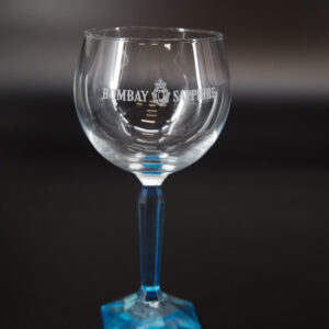 Calice da gin Bombay Sapphire in vetro trasparente con logo inciso, stelo e base blu sfaccettati, su sfondo scuro.