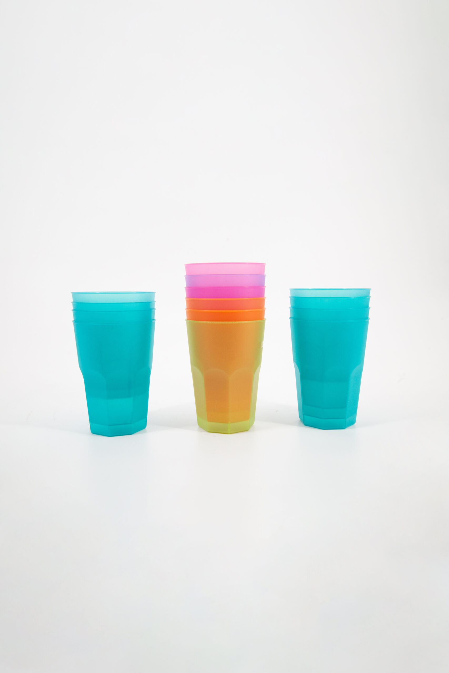 Tre pile di bicchieri in plastica riutilizzabili e colorati su sfondo bianco. Due pile sono turchesi, una centrale è multicolore.