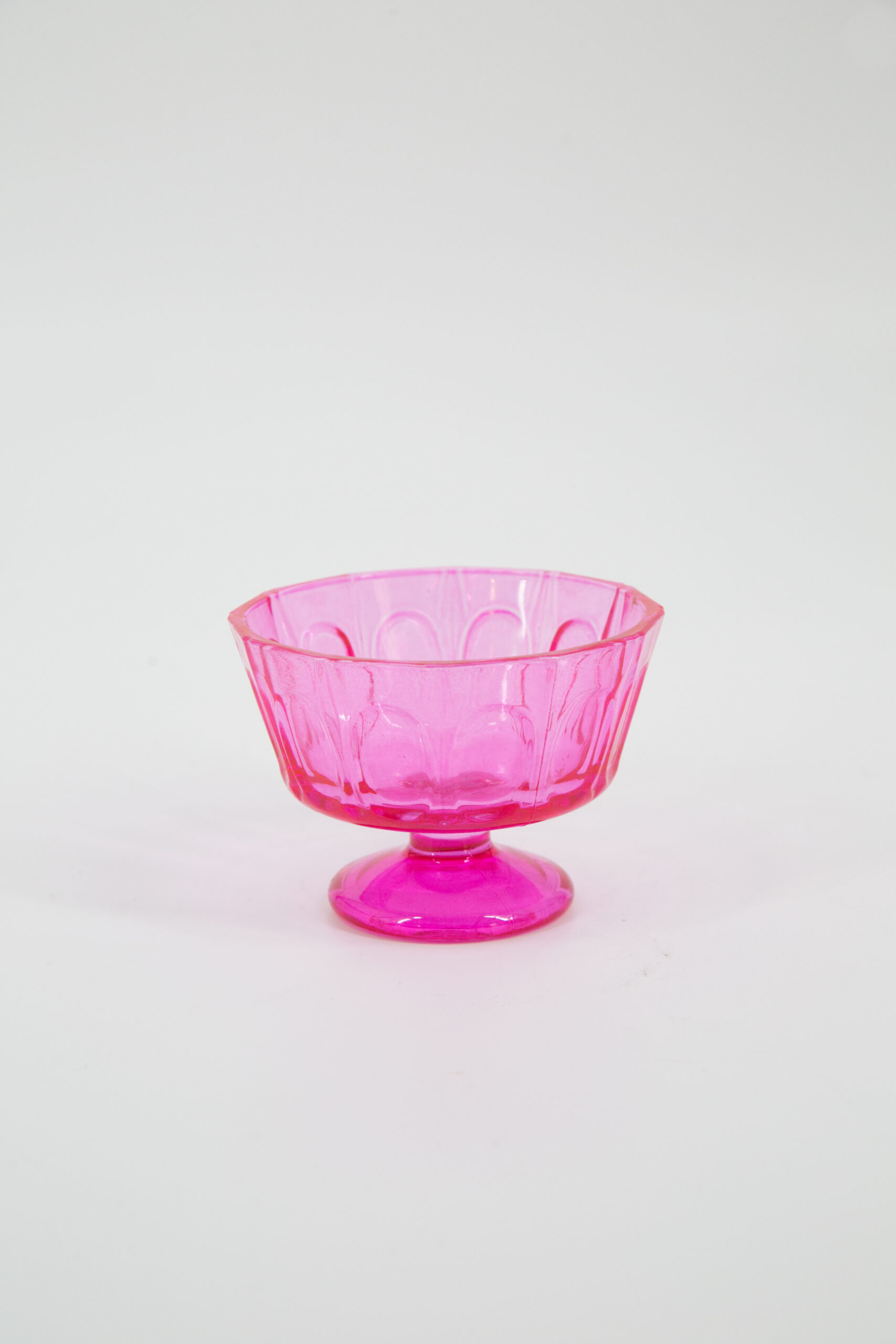 Coppetta decorativa in vetro o plastica traslucida di colore rosa intenso, con superficie sfaccettata e piedistallo, su sfondo bianco.