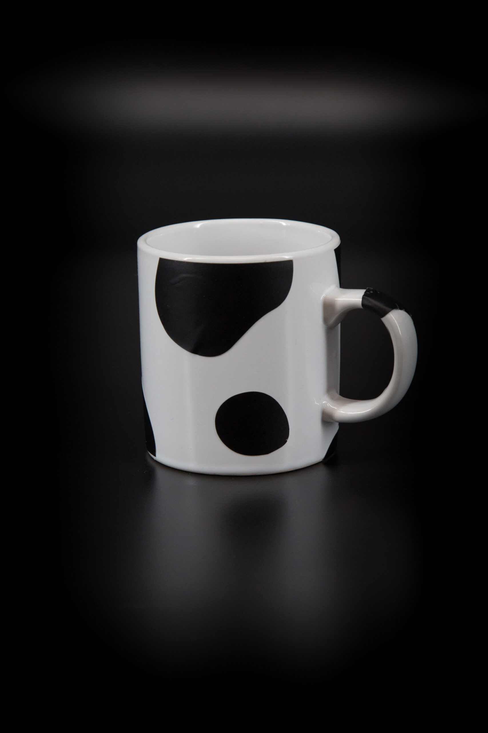 Tazza in ceramica bianca con grandi macchie nere irregolari, simile al manto di una mucca, su sfondo scuro.