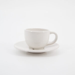 Una tazzina da caffè in ceramica bianca con il suo piattino coordinato, fotografata su sfondo neutro.