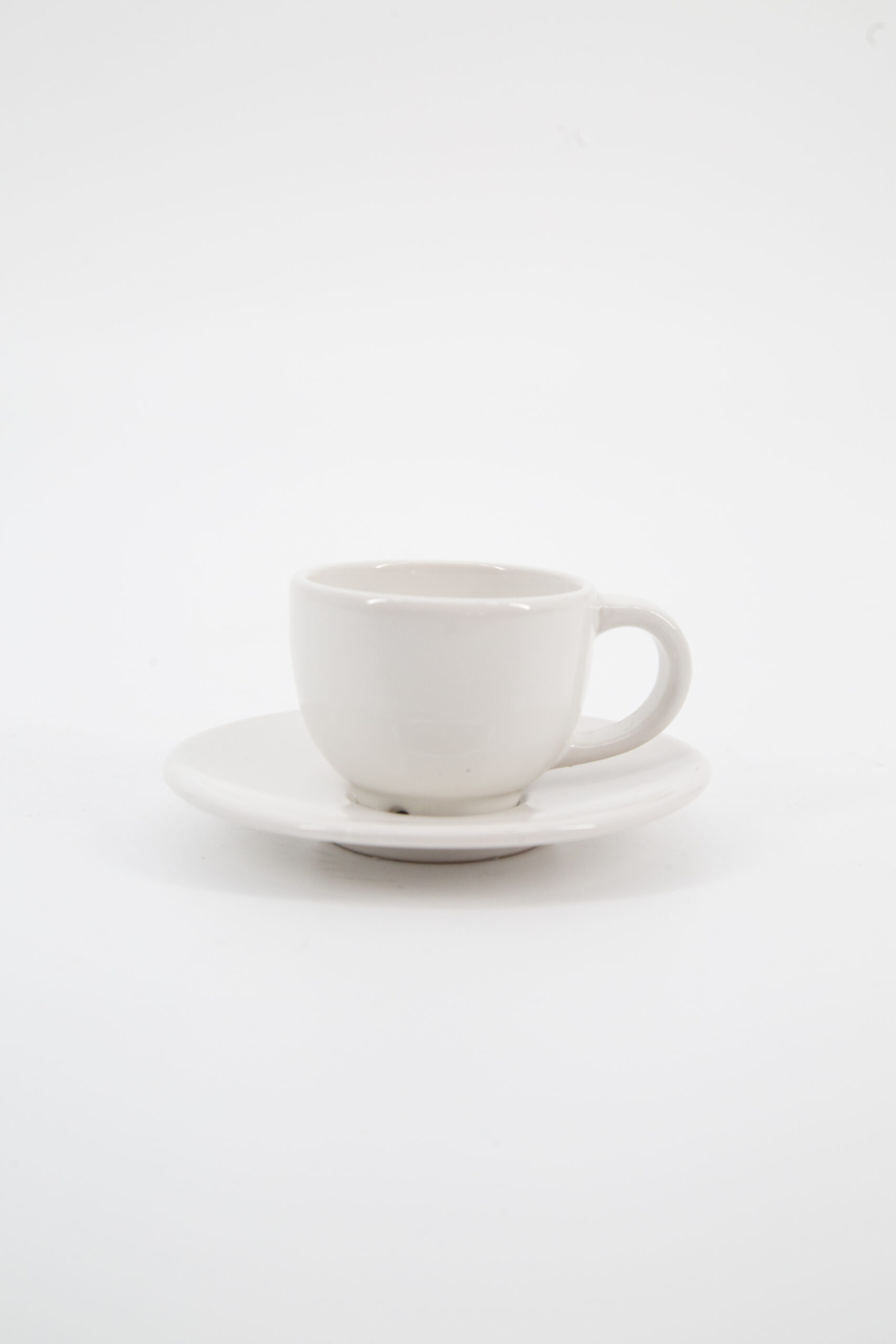 Una tazzina da caffè in ceramica bianca con il suo piattino coordinato, fotografata su sfondo neutro.