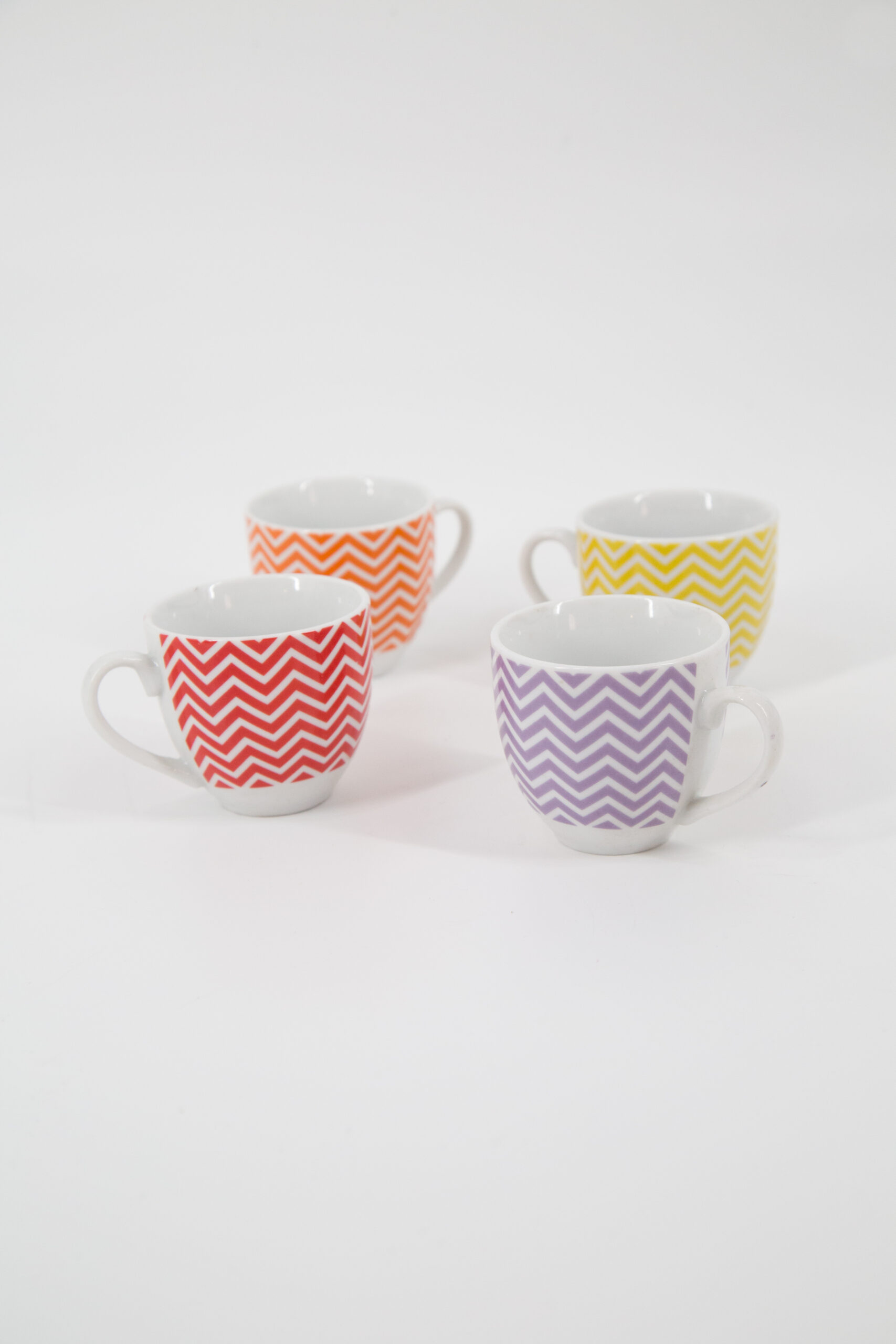 Quattro tazzine in ceramica con motivo chevron rosso, arancione, giallo e viola, disposte su sfondo bianco.