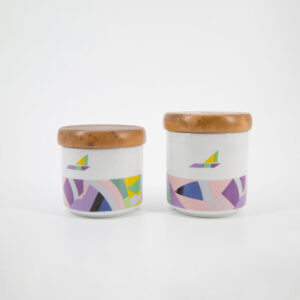 Due contenitori cilindrici in ceramica bianca con coperchi in legno e decorazioni astratte multicolori, su sfondo bianco.