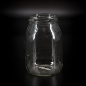Un vaso in vetro trasparente vuoto, con collo filettato, fotografato frontalmente su uno sfondo scuro e sfumato.