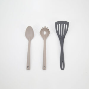 Tre utensili da cucina in silicone, un mestolo, una forchetta per spaghetti e una paletta forata, su sfondo bianco.