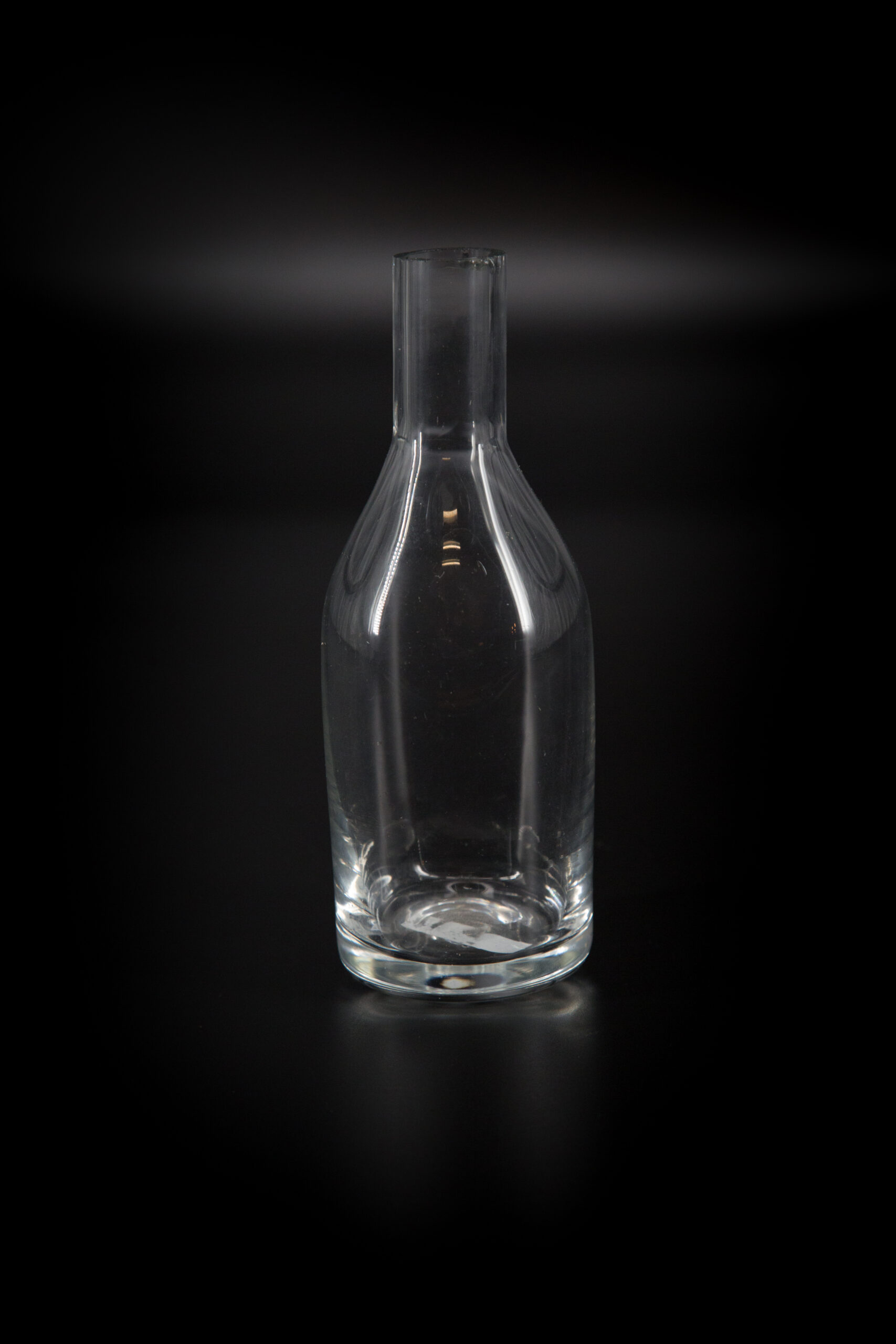 Caraffa in vetro trasparente con collo stretto e corpo cilindrico, fotografata su sfondo nero, ideale come oggetto di scena.