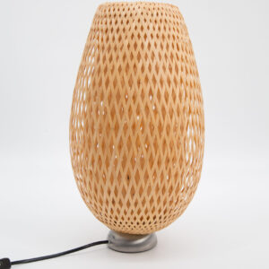 Lampada da tavolo con paralume in bambù intrecciato a trama diagonale e base metallica, su sfondo bianco.