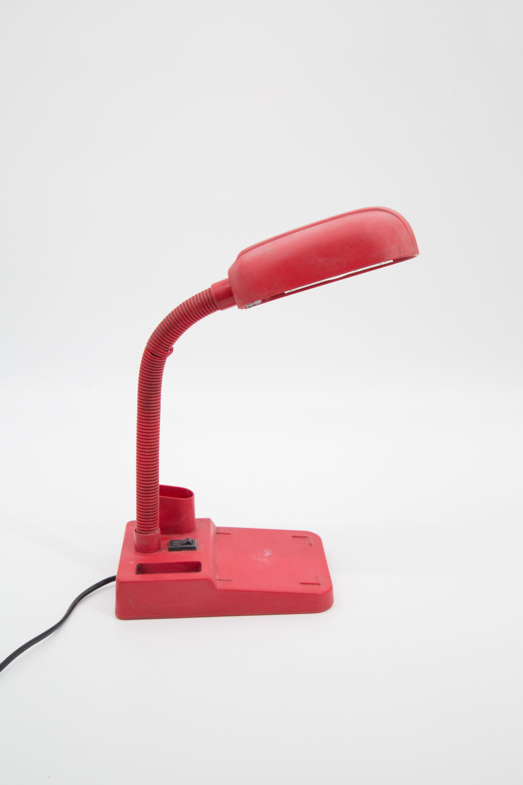 Lampada da scrivania rossa con braccio flessibile e base rettangolare, vista laterale su sfondo bianco.