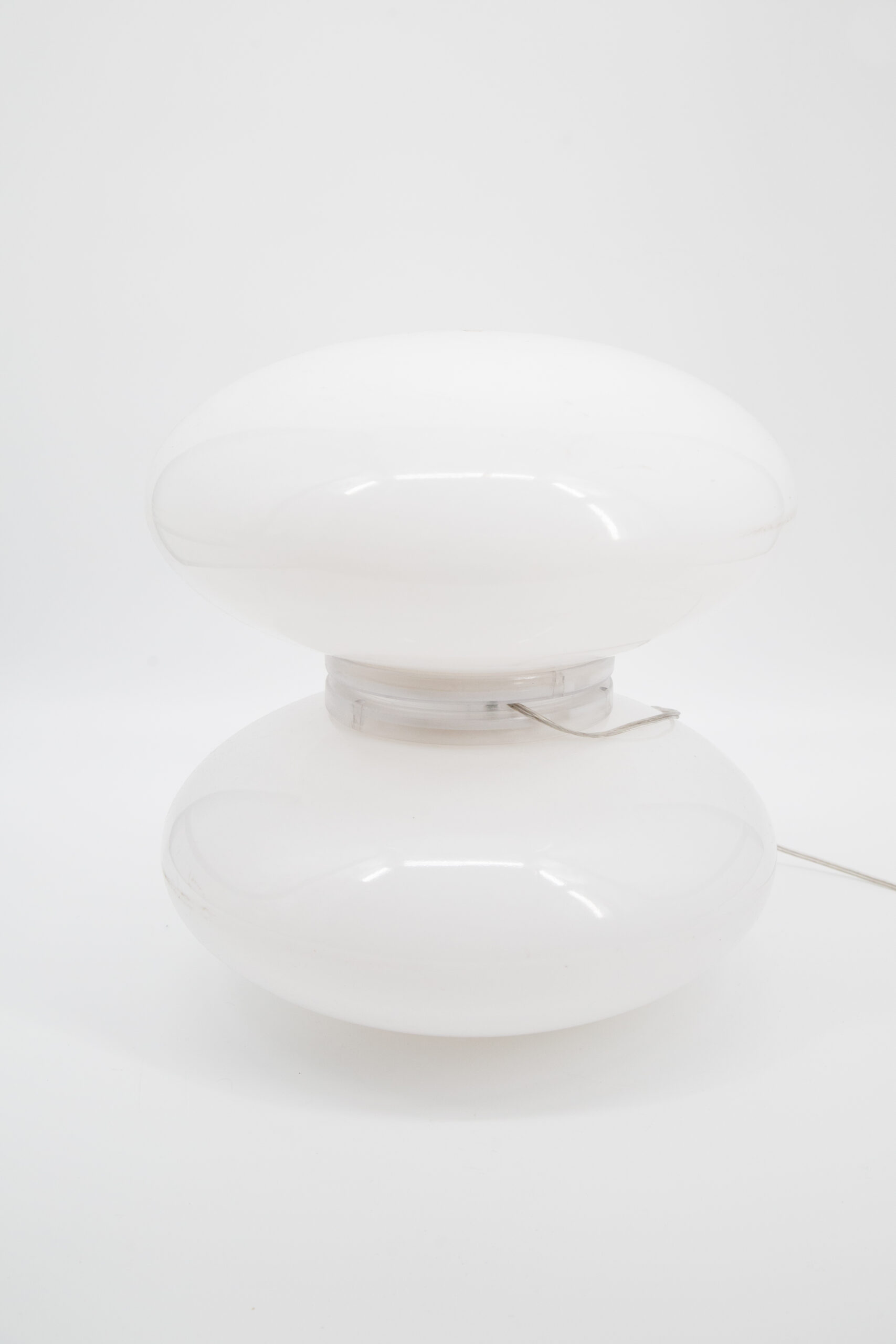 Lampada da tavolo bianca lucida a forma di fungo, con due sezioni ellissoidali sovrapposte e base trasparente, su sfondo bianco.
