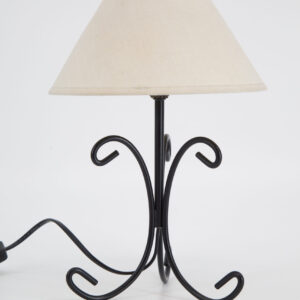 Lampada da tavolo con base in ferro battuto nero e paralume conico in tessuto ecrù, su sfondo bianco.