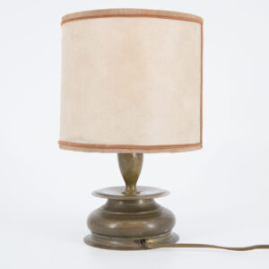 Lampada da tavolo vintage con base in metallo patinato e paralume cilindrico in tessuto beige, su sfondo bianco.