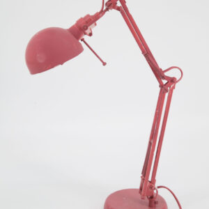 Lampada da tavolo orientabile di colore rosso, con braccio snodabile e base circolare, su sfondo bianco. Presenta segni di usura che ne accentuano il carattere vintage.