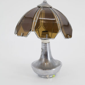 Lampada da tavolo vintage con base cromata lucida e paralume a cupola composto da pannelli traslucidi color ambra incorniciati in metallo.