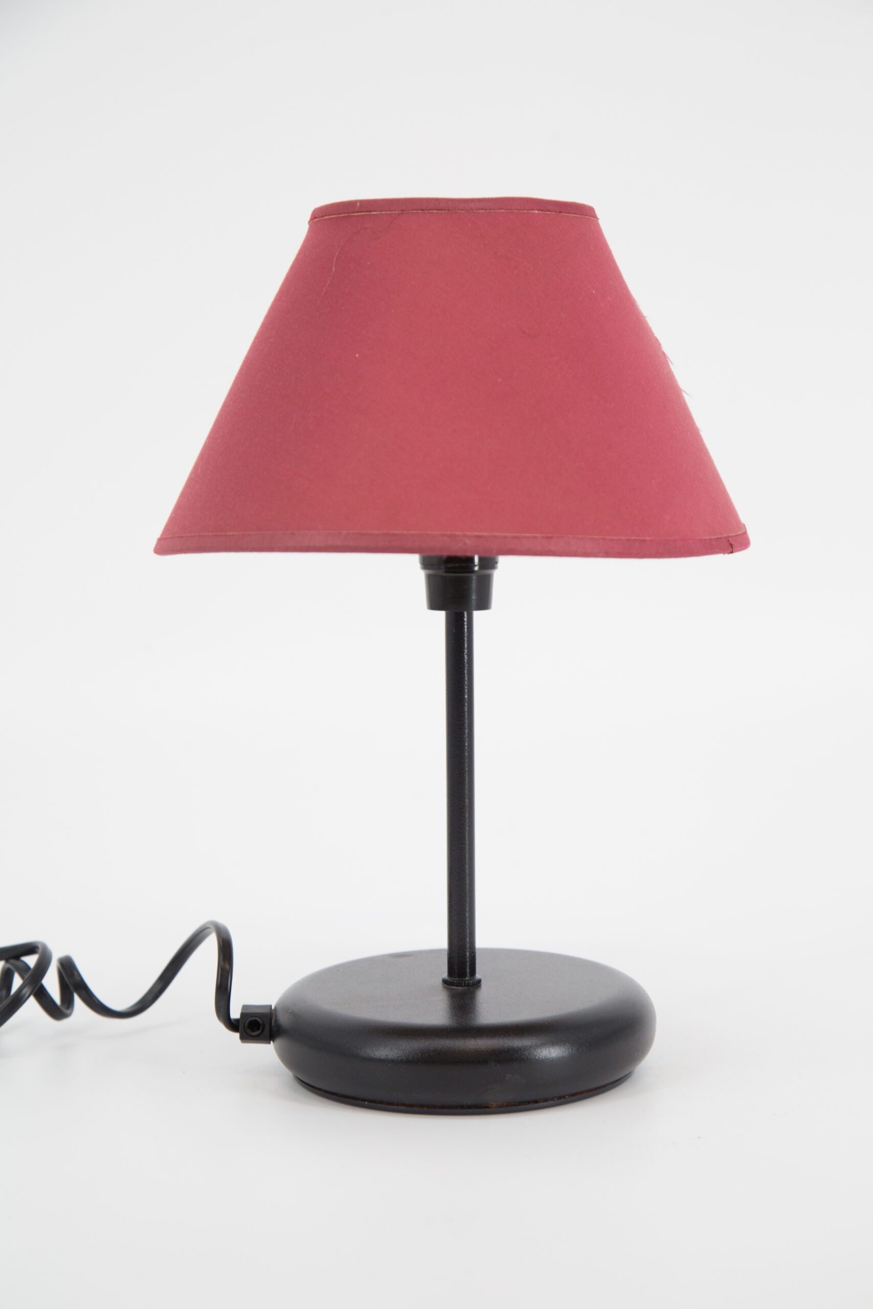Lampada da tavolo con base e stelo neri e paralume conico in tessuto rosso bordeaux su sfondo bianco.