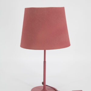 Lampada da tavolo monocromatica rosa antico con paralume in tessuto e base in metallo, interruttore sul cavo, su sfondo bianco.
