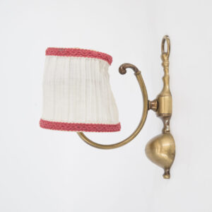 Applique da parete vintage in ottone con braccio curvo e paralume plissettato in tessuto bianco con bordo rosso.