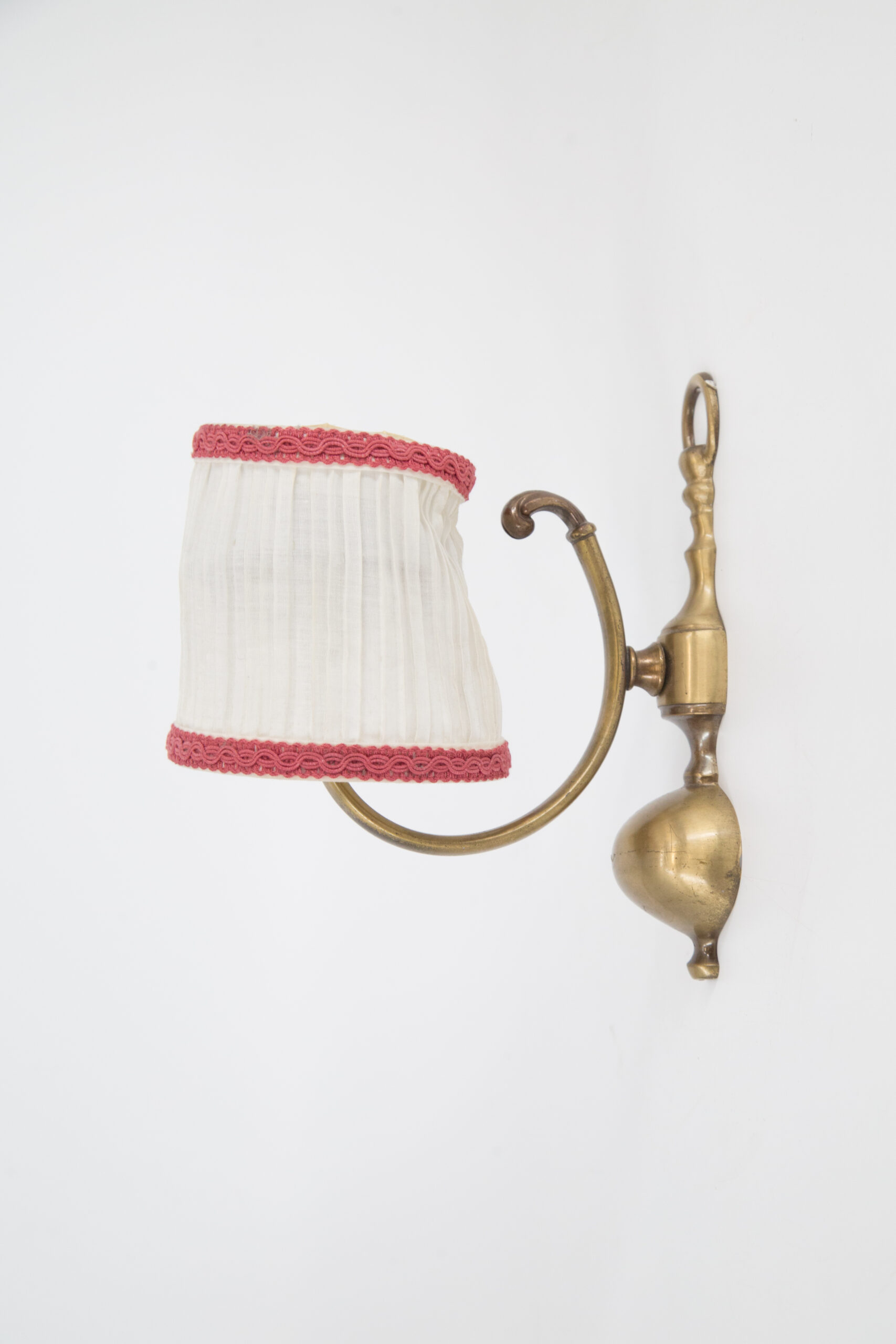 Applique da parete vintage in ottone con braccio curvo e paralume plissettato in tessuto bianco con bordo rosso.