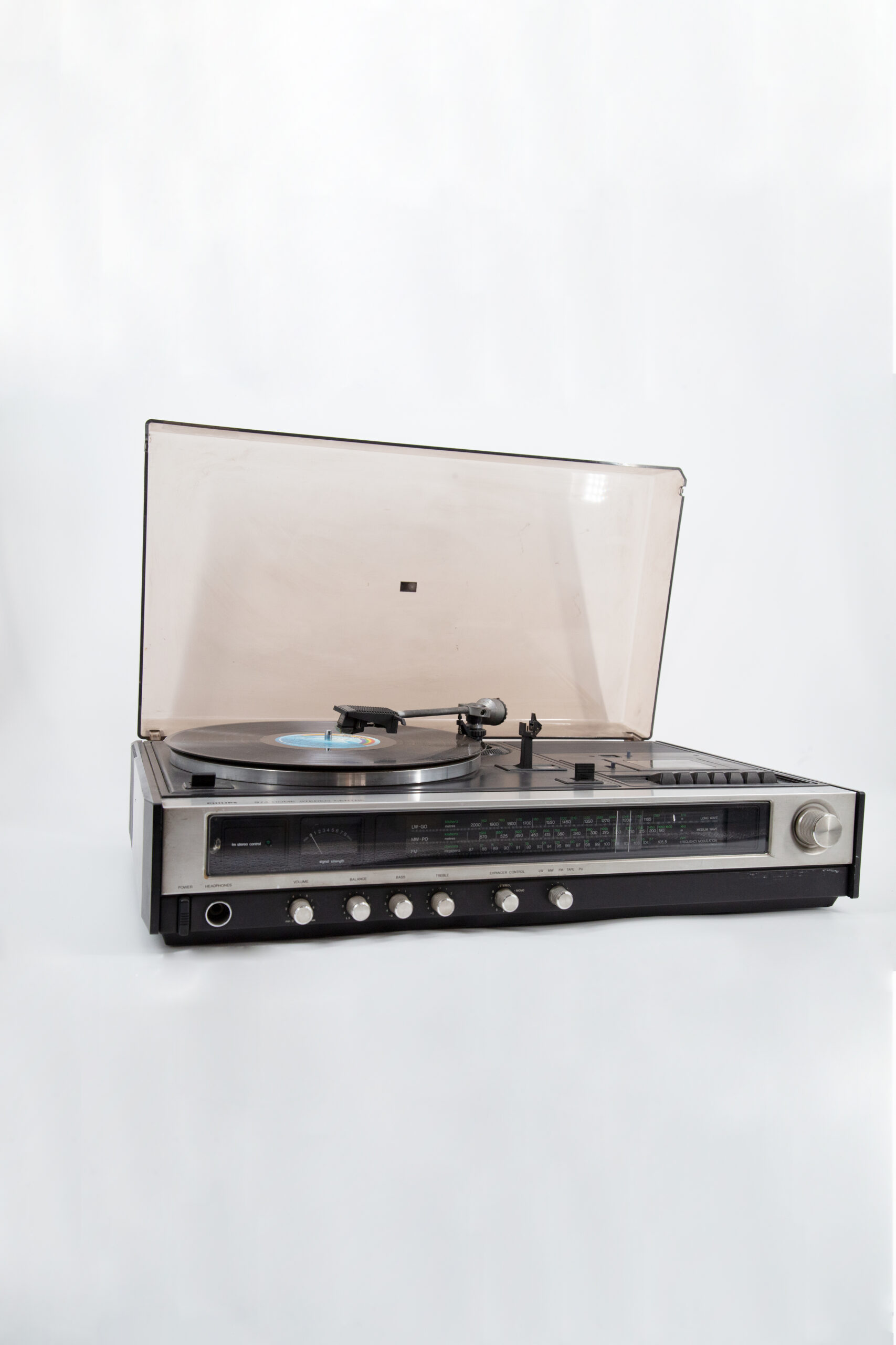 Un centro stereo vintage Philips nero e argento con giradischi, radio e coperchio antipolvere aperto, su sfondo bianco.