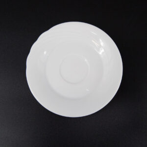 Sottotazza rotondo in ceramica bianca lucida, con bordo leggermente ondulato, posizionato su uno sfondo nero. Vista dall'alto.