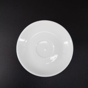 Un sottotazza bianco in ceramica, di forma circolare e con una leggera rientranza centrale, su sfondo nero.