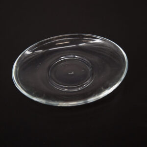 Piattino sottotazza in vetro trasparente, di forma circolare e design minimalista, posizionato su uno sfondo nero.