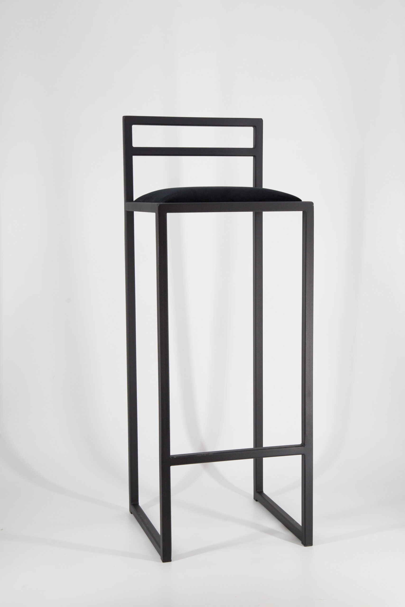 Sgabello da bar alto con struttura in metallo nero opaco e seduta imbottita in velluto nero, su sfondo bianco.