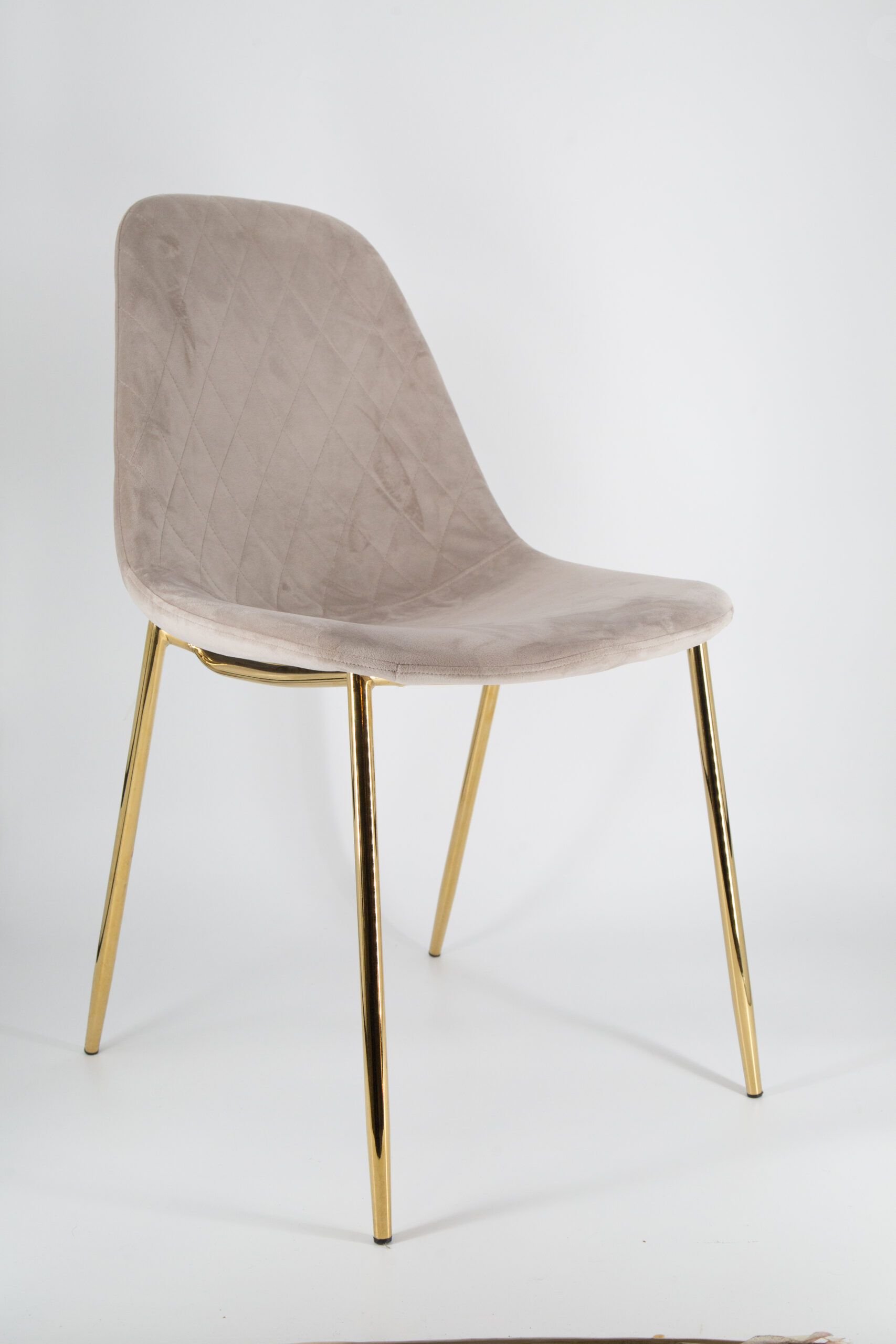 Sedia moderna imbottita in tessuto vellutato color beige chiaro con trapuntatura a rombi sullo schienale e gambe sottili in metallo dorato lucido, su sfondo bianco.