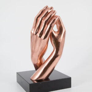 Scultura decorativa di due mani giunte con finitura metallica color rame lucido, montata su una base rettangolare nera.