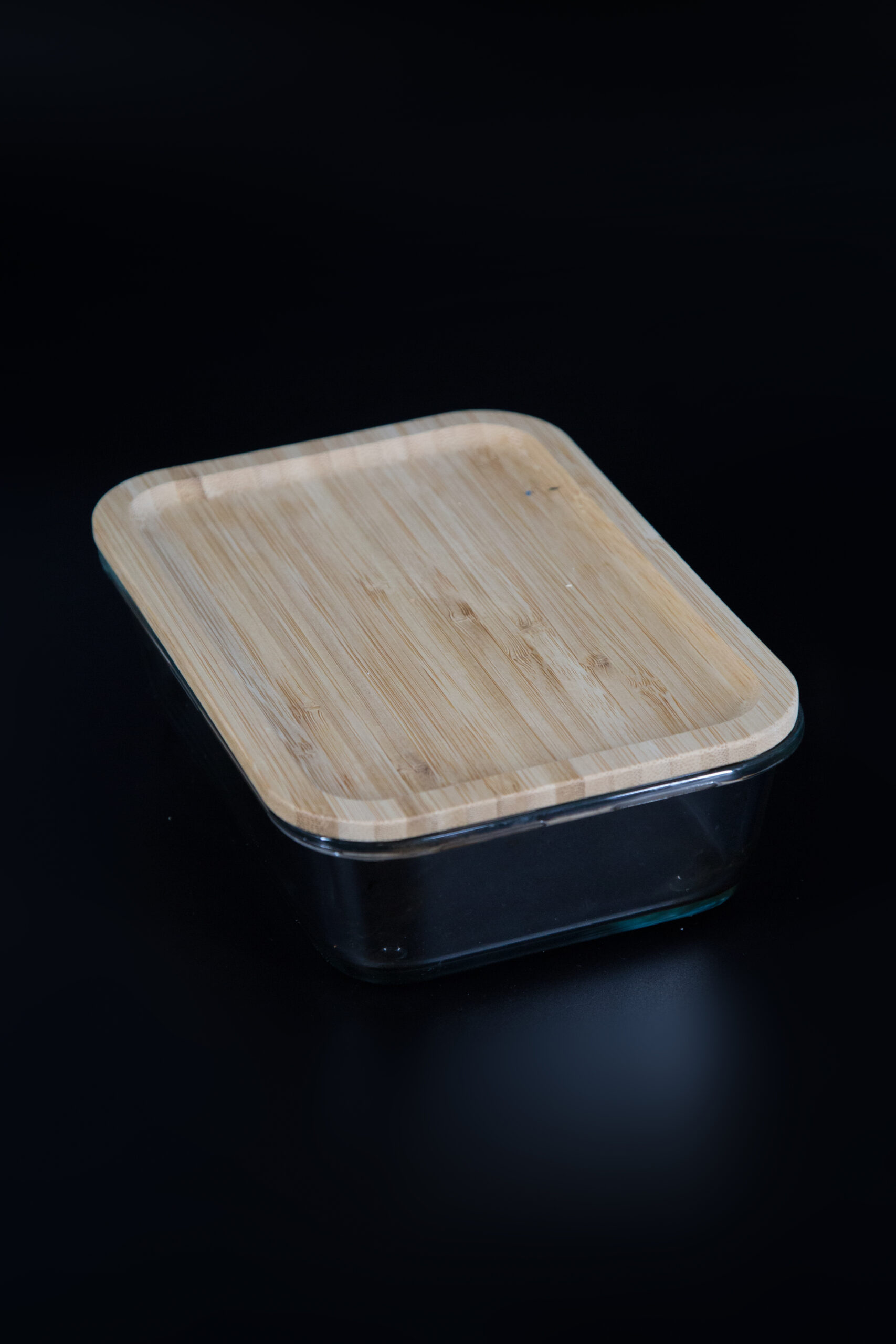 Contenitore in vetro rettangolare trasparente con coperchio in legno di bambù chiaro, posizionato su sfondo nero.