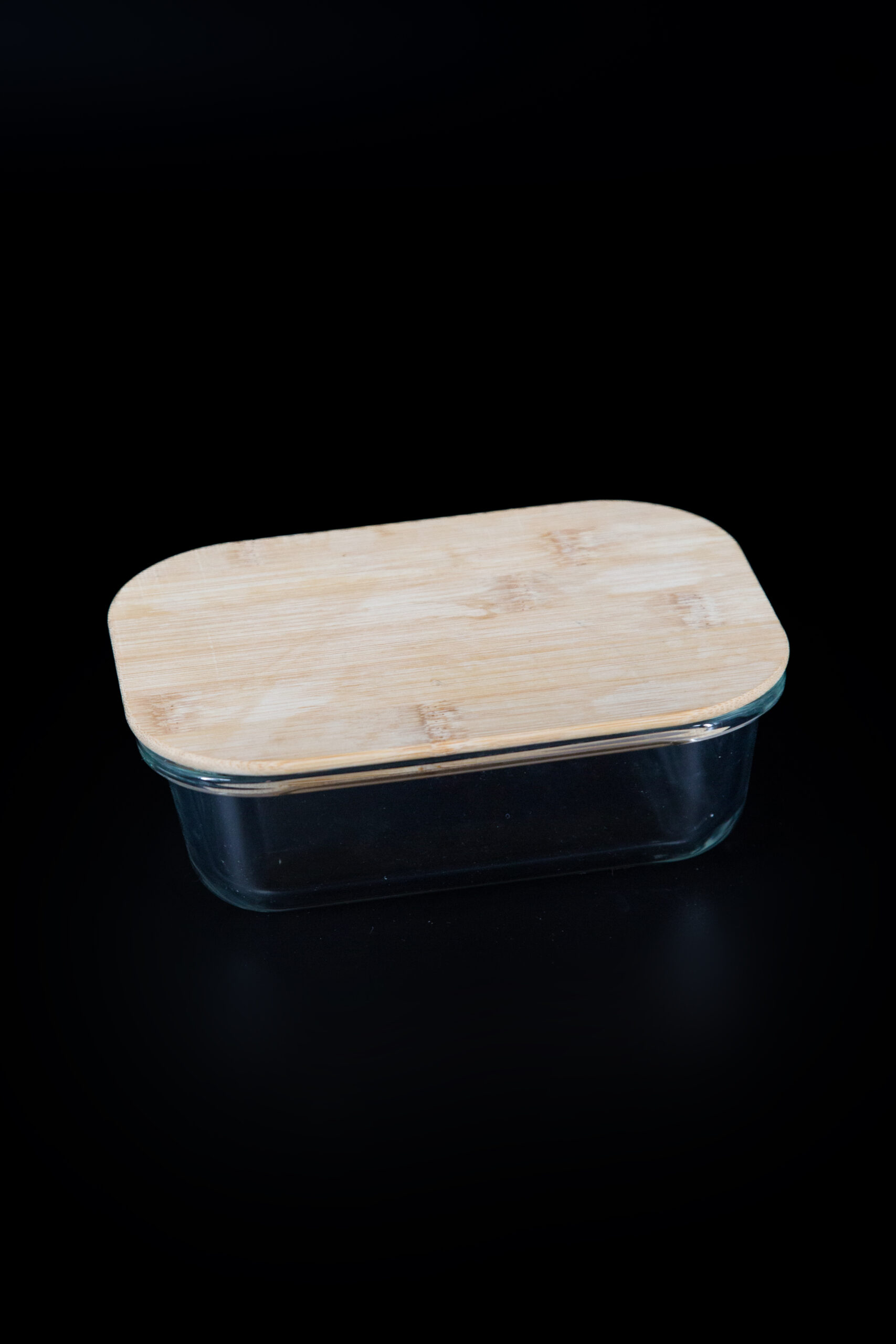 Contenitore rettangolare in vetro trasparente con coperchio in legno di bambù chiaro, posizionato su sfondo nero.