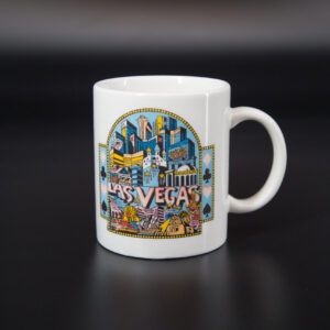 Tazza in ceramica bianca con stampa colorata dello skyline di Las Vegas e simboli delle carte da gioco, su sfondo nero.