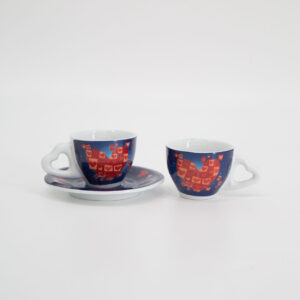 Due tazzine da caffè in ceramica con manici a cuore e decoro a cuori rossi su sfondo blu, una con piattino, su sfondo bianco.
