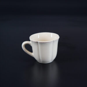 Tazza in ceramica color crema con design a coste verticali e bordo leggermente anticato, su sfondo scuro.