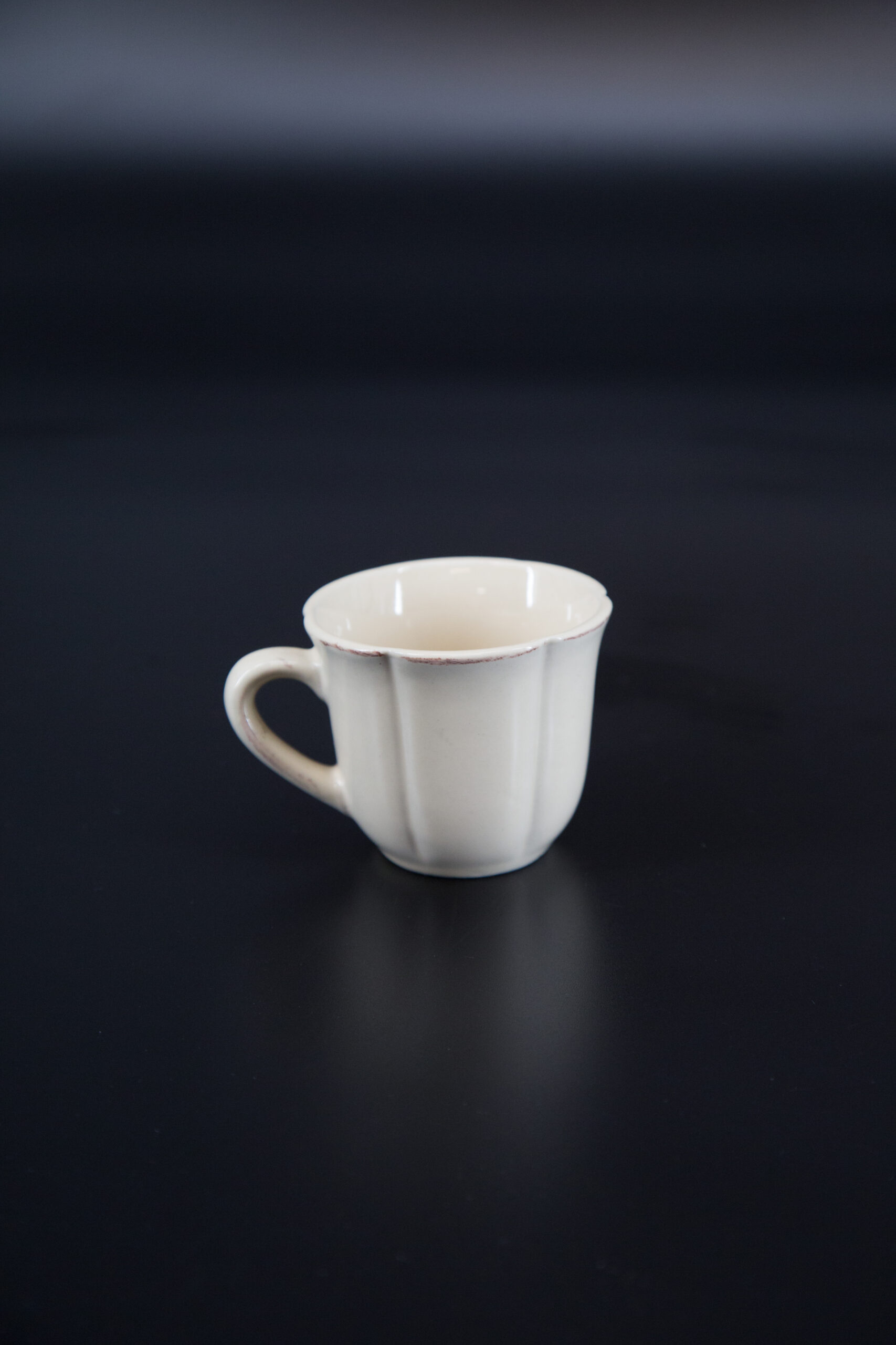 Tazza in ceramica color crema con design a coste verticali e bordo leggermente anticato, su sfondo scuro.