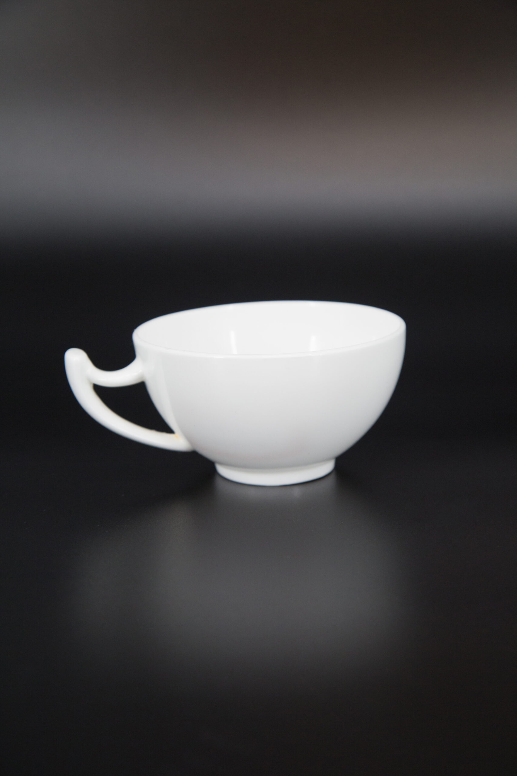 Tazza bianca opaca con manico curvo e design minimalista, fotografata su sfondo scuro.