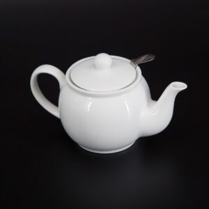 Teiera in ceramica bianca lucida con coperchio e infusore in metallo, posizionata su sfondo nero.
