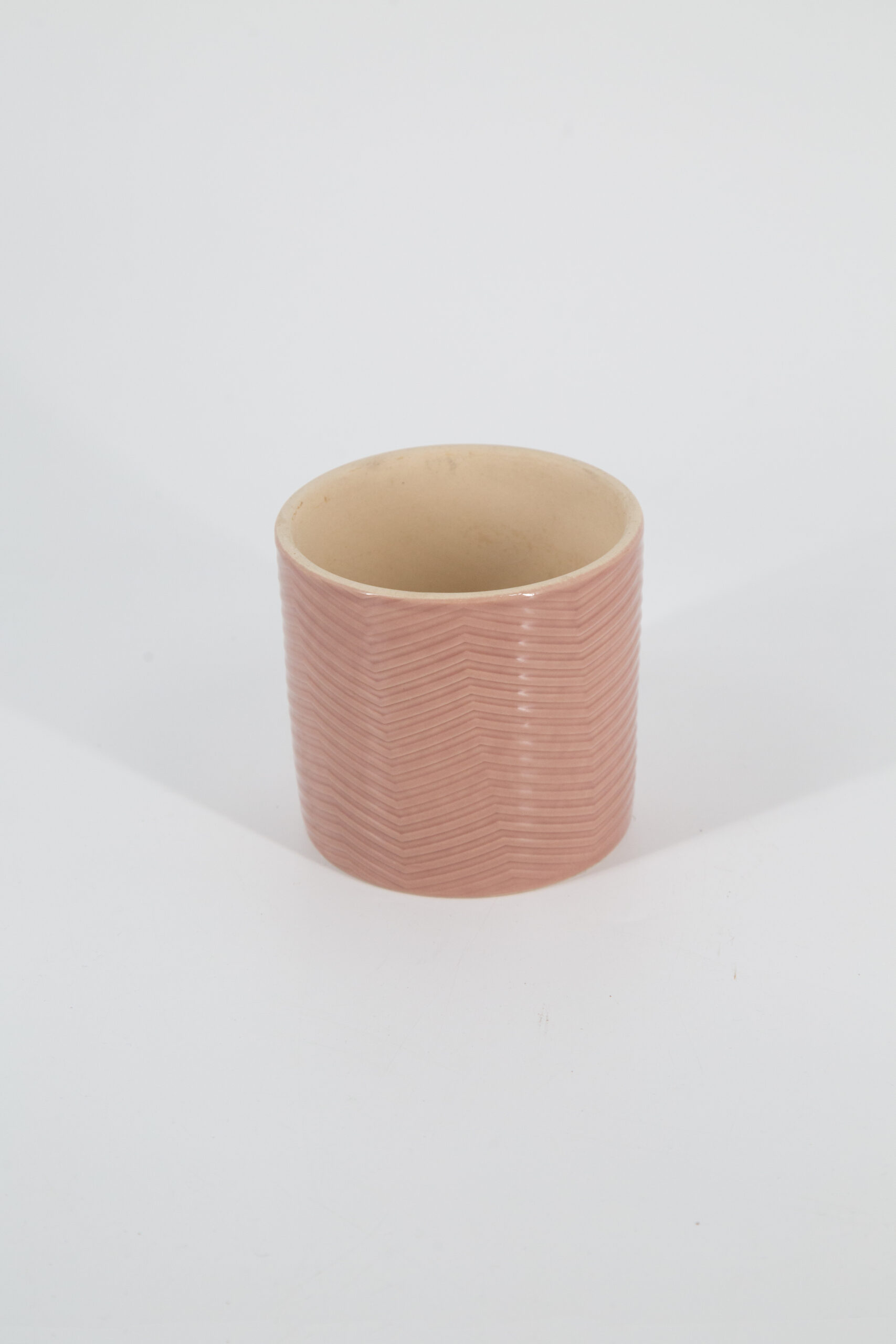 Vaso cilindrico in ceramica rosa tenue con superficie testurizzata a motivo zigzag, interno beige, su sfondo bianco.