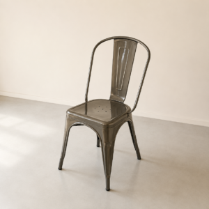 Sedia industriale in metallo scuro, stile Tolix, con schienale curvo e seduta forata, su pavimento chiaro in un ambiente minimalista.