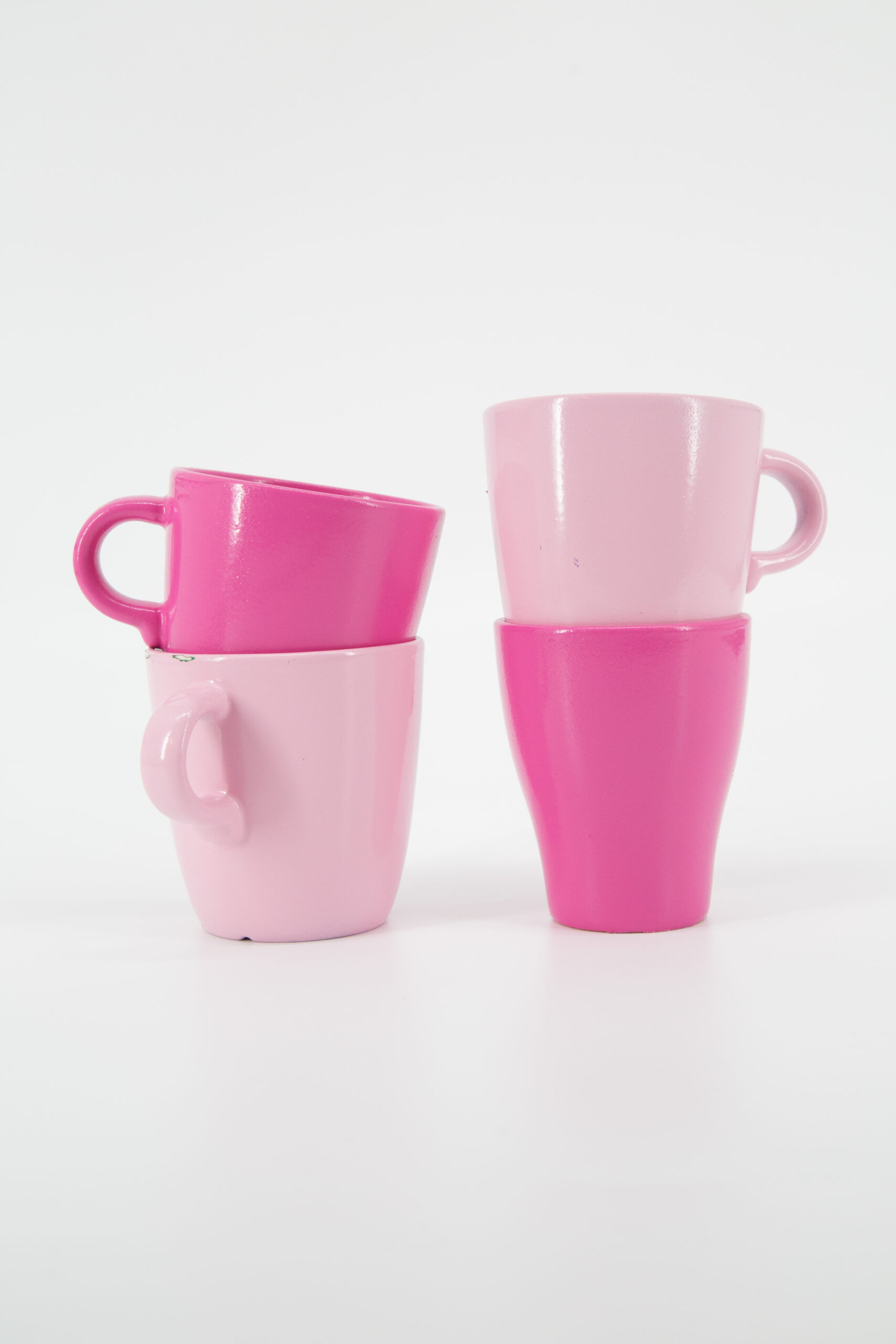 Quattro tazze in ceramica, due rosa chiaro e due fucsia, impilate a coppie su sfondo bianco, ideali come oggetti di scena.