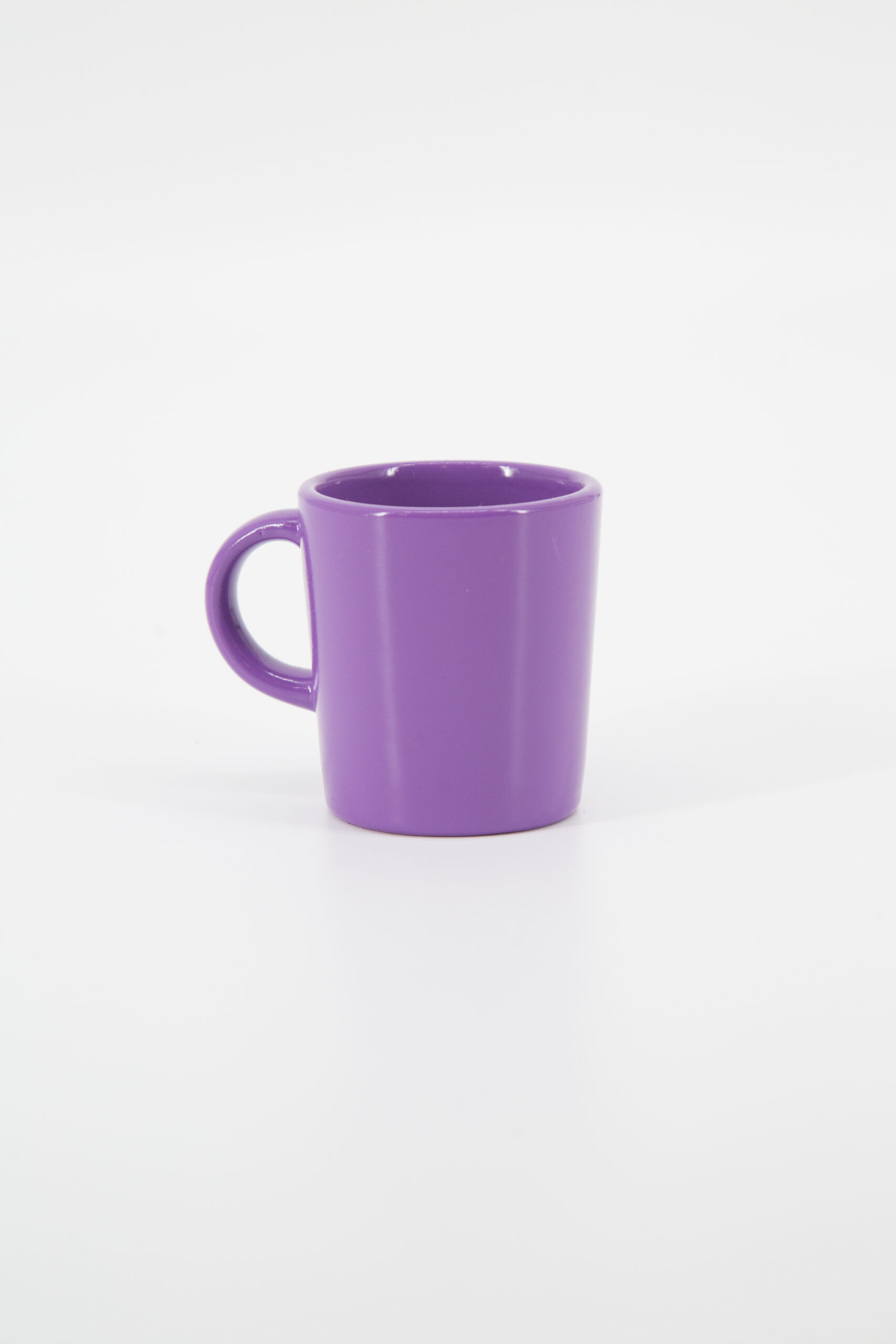 Un mug in ceramica di colore viola intenso, con manico, posizionato su uno sfondo bianco neutro.